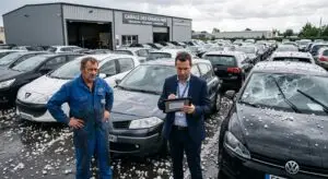 Un expert en assurance examine les dégâts causés par la grêle sur un parc de voitures en présence d'un garagiste couvert par une RC Pro Garage.